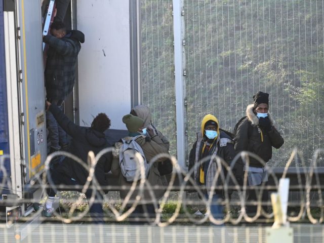 Migrant climb into the back of lorries bound for Britain while traffic is stopped upon waiting to board shuttles at the entrance to the Channel Tunnel site in Calais, northern France, on December 10, 2020. - The French port of Calais continues to attract migrants from the Middle East and …