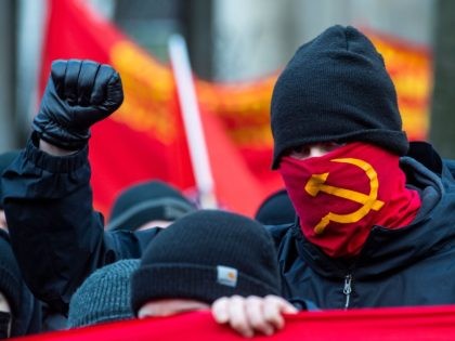 A protester wearing a face mask with a hammer and sickle symbol raises his fist during a yearly demonstration held by various leftist parties and organisations to commemorate the assassination of Communist icons Rosa Luxemburg and Karl Liebknecht in 1919, in Berlin on January 10, 2021. - Scores of demonstrators …