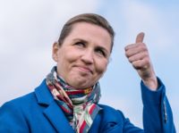 Denmark's Prime Minister Mette Frederiksen reacts with a thumb up as she stands on a boat with wind turbines of the Middelgrunden offshore wind farm in the background, in Oeresund between Denmark and Sweden, outside Copenhagen, on April 22, 2021. - During this trip HOFOR (Greater Copenhagen Utility), who's aim …