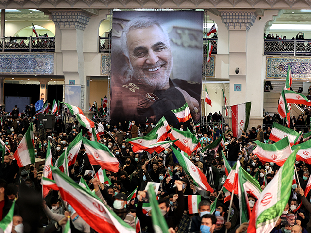Iranians lift national flags during a ceremony in the capital Tehran, on January 3, 2022, commemorating the second anniversary of the killing in Iraq of top Iranian commander Qasem Soleimani (portrait) and Iraqi commander Abu Mahdi al-Muhandis in a US raid. (Photo by ATTA KENARE / AFP) (Photo by ATTA KENARE/AFP via Getty Images)