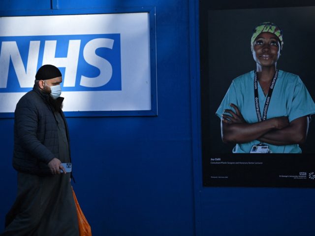 Pedestrians walk past images of workers of Britain's National Health Service (NHS) fixed to hoardings outside a temporary field hospital, set up in the grounds of St George's Hospital in Tooting, south London on January 5, 2022. - Britain's state-run National Health Service (NHS) is struggling with staff forced to …