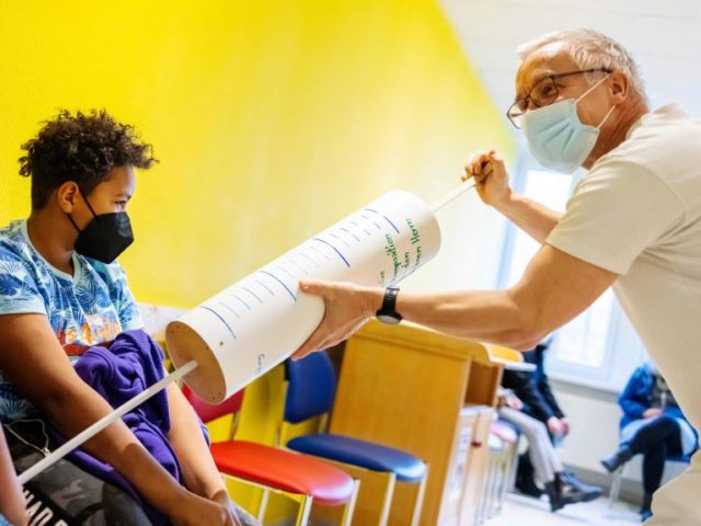 Paediatrician Steffen Lueder (R) jokes with children using an oversized syringe during a v