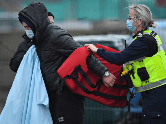 A UK Immigration Enforcement officer helps a migrant, picked up at sea attempting to cross the English Channel, remove his life jacket on arrival at the Marina in Dover, southeast England, on January 10, 2022. - Last year, record numbers of more than 28,000 migrants who paid thousands of pounds …