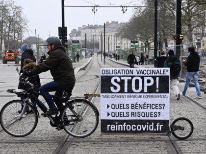 A man displays a banner, promoting the alleged conspiracy theory website 'reinfocovid', as he rides a bike during a rally to protest against the health pass and Covid-19 vaccines in Nantes, western France on January 15, 2022. (Photo by DAMIEN MEYER / AFP) (Photo by DAMIEN MEYER/AFP via Getty Images)