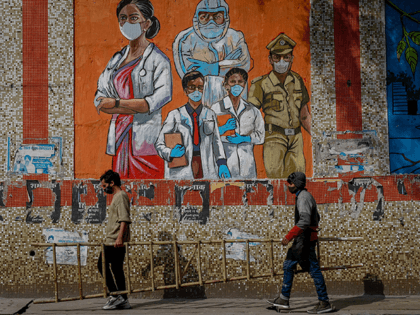Graffiti artists walk off carrying a ladder they used to draw a mural based on Covid-19 coronavirus safety protocols on the walls of an underpass during an ongoing weekend curfew imposed in New Delhi on January 16, 2022 to curb the spread of the Covid-19 coronavirus. (Photo by Sajjad HUSSAIN …