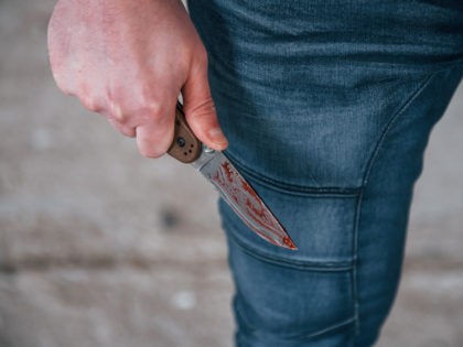 Close up view of killer that standing with knive with blood in hand.