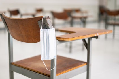 A used medical facemask hangs on a wood lecture chair in the empty classroom during the CO