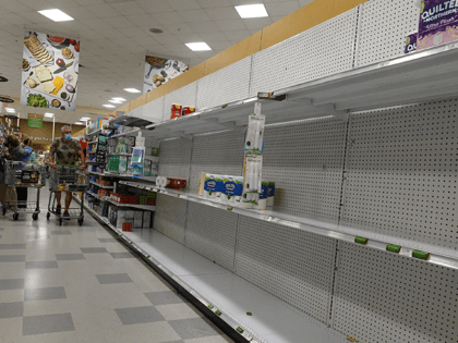 A shelf displaying toilet paper sits almost empty as shoppers makes their way through a su
