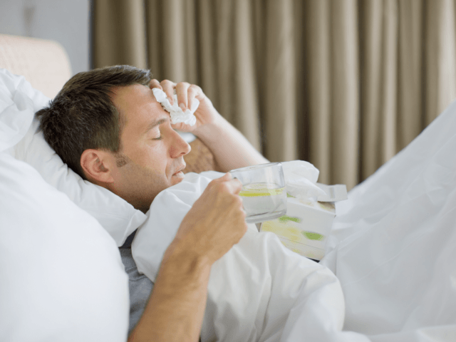 Man sick in bed drinking hot drink - stock photo
