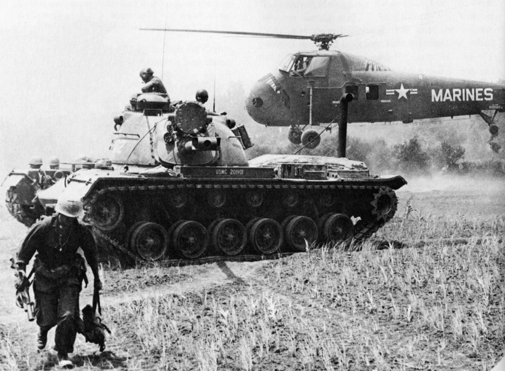 A MAG-16 helicopter evacuates casualties, while a Marine M48 Patton tank stands guard