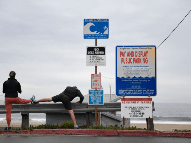 People stretch next to a tsunami hazard zone sign in El Segundo, California, on January 15, 2022. - The US National Weather Service issued tsunami advisories for the entire west coast of the United States following a massive volcanic eruption across the Pacific Ocean in Tonga. (Photo by Patrick T. …