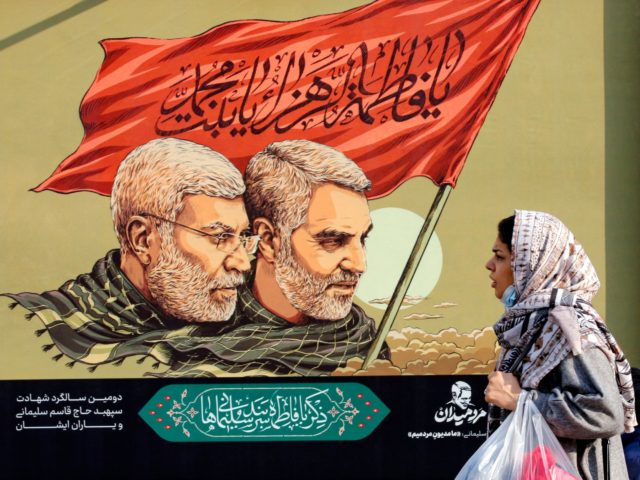An Iranian woman walks past a large poster of slain top Iranian general Qasem Soleimani (R