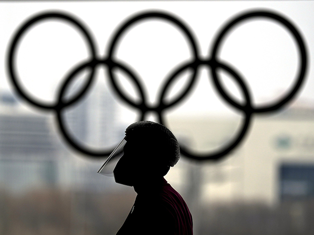 A person wearing a face shield walks past the Olympic rings inside the main media center a
