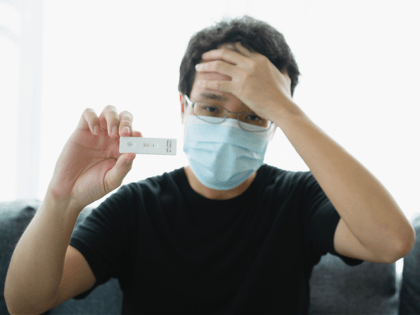 Unrecognizable Asian young man with face mask using COVID-19 or 2019 SARS-nCoV antigen rapid self test at home during the quarantine, ag test result shown positive.