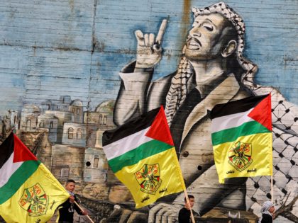 TOPSHOT - Masked members of the Fatah movement walk with flags of Palestine and Fatah past a mural depicting late Palestinian leader Yasser Arafat during a rally in solidarity with hunger-striking Palestinian prisoner Hisham Abu Hawash, in the city of Nablus in the north of the occupied West Bank on …