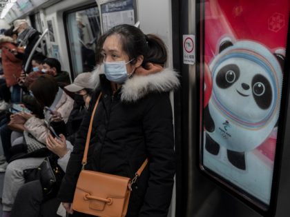 BEIJING, CHINA - JANUARY 13: A woman wears a protective mask as they ride on a metro car next to a logo for Beijing 2022 Winter Olympics mascot Bing Dwen Dwen during rush hour on January 13, 2022 in Beijing, China. While China has mostly contained the spread of COVID-19 …