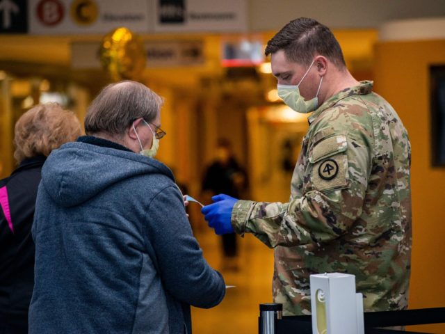 A soldier helps welcome visitors in the lobby handing out new masks and visitor stickers at UMass Memorial Medical Center in Worcester, Massachusetts on December 30, 2021. - The Massachusetts National Guard has activated up to 500 soldiers and airmen to help address the medical worker shortage at 55 hospitals and …