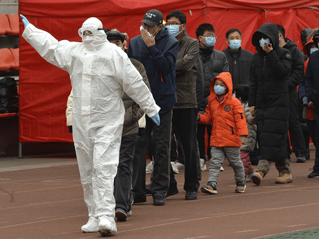 A worker wearing a protective suit gestures to a line of people at a COVID-19 testing site
