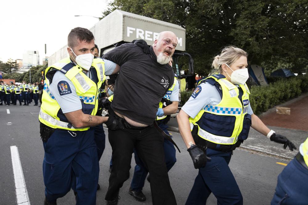 A man is arrested as police and protesters clash in Wellington, New Zealand, Tuesday, Feb. 22, 2022, as police tightened a cordon around a protest convoy that has been camped outside Parliament for two weeks. The protesters, who oppose coronavirus vaccine mandates and were inspired by similar protests in Canada, appear fairly well organized after trucking in portable toilets, crates of donated food, and bales of straw to lay down when the grass turned to mud. (George Heard/New Zealand Herald via AP)