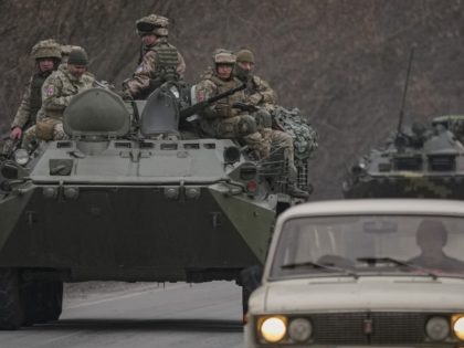 Ukrainian servicemen sit atop armored personnel carriers driving on a road in the Donetsk