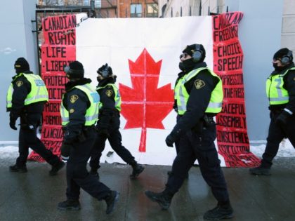 A group of police officers walk past a Canadian flag near Parliament Hill as demonstrators continue to protest the vaccine mandates implemented by Prime Minister Justin Trudeau on February 7, 2022 in Ottawa, Canada. - Canadian authorities struggled Monday to tackle a truckers' protest against Covid restrictions which has paralyzed …