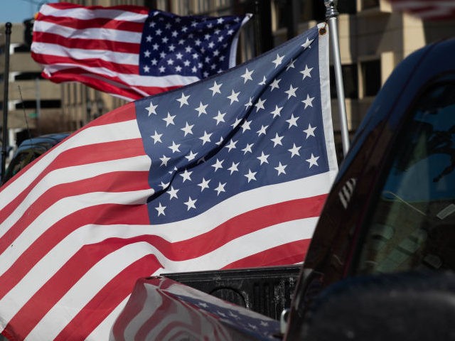 American flags blow in the mind as cars line up to participate in a Freedom Convoy protesting Covid restrictions and demanding election audits on February 20, 2022 in Lansing, Michigan. The Freedom Convoy has been circling the Michigan State Capitol daily while simultaneously honking horns in support of ongoing protests …