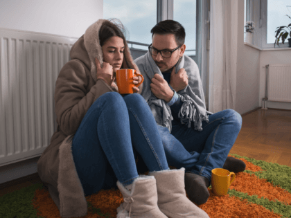 Couple sitting beside radiator - stock photo Young couple in jacket and covered with blanket sitting on floor beside radiator and trying to warm up