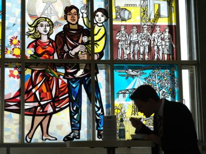 BERLIN, GERMANY - MARCH 19: A participant at the Global Solutions Summit eats next to a communist-era, stained glass Socialist Realist mural by artist Walter Womacka at the European School of Management and Technology on March 19, 2019 in Berlin, Germany. The building that houses the ESMT today was once …