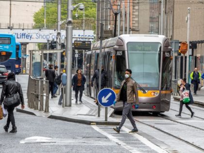 People cross the tram tracks in Dublin City centre in Ireland on May 18, 2020, as Ireland cautiously begins to lift it's coronavirus lockdown. - Ireland launched the first tentative step in its plan to lift coronavirus lockdown on Monday, with staff returning to outdoor workplaces as some shops resumed …