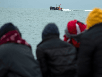 Migrants sitting on the beach look on as an RNLI (Royal National Lifeboat Institution) lifeboat carrying migrants approaches a beach in Dungeness on the south-east coast of England on November 24, 2021, after being rescued while crossing the English Channel. - The past three years have seen a significant rise …