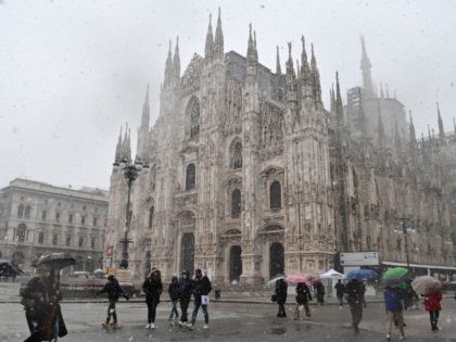 People walks across Piazza del Duomo past the cathedral as snow falls in Milan on December