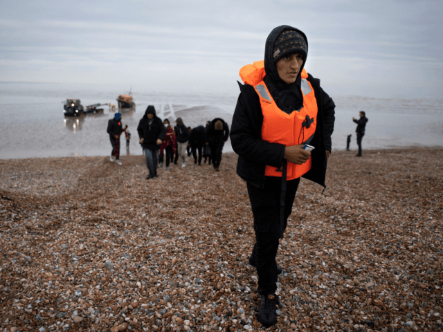 Migrants walk on a beach after being helped ashore by an RNLI (Royal National Lifeboat Institution) lifeboat in Dungeness on the southeast coast of England on December 16, 2021. - A report by prison inspectors and independent monitors has found that conditions for migrants detained on the Kent coast after …