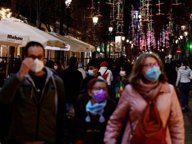 Passers-by, wearing a face mask as a protection against Covid-19, walk past Christmas lights in the streets of Madrid, on December 22, 2021. - Spain will reimpose a nationwide rule requiring the use of face masks outdoors, the government said on December 22, 2021, as the country grapples with a …