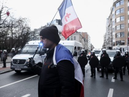Belgian riot police stand behind a protester with a French flag bearing the Cross of Lorraine as participants of the so-called "Freedom Convoy" (Convoi de la Liberte) take part in an unauthorised demonstration in the center of Bruxelles on February 14, 2022 to protest against coronavirus disease (COVID-19). - Belgian …