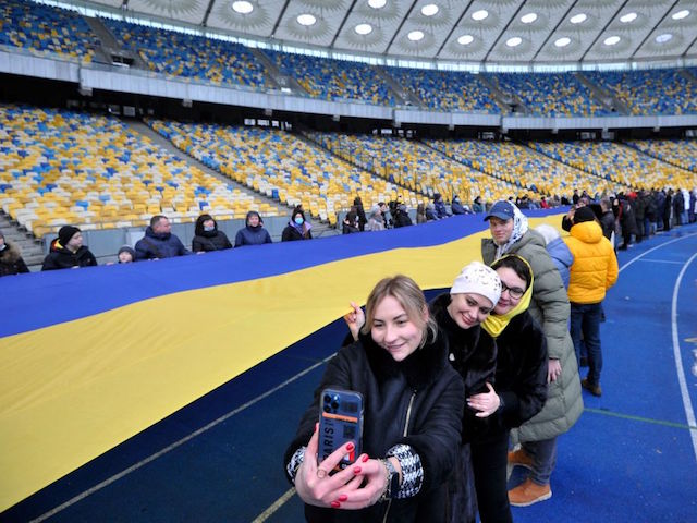 People take pictures as they carry a giant Ukraine's national flag at a stadium to mark a "Day of Unity" in Kyiv on February 16, 2022. - Ukrainian leaders were to stage a "Day of Unity" on February 16, 2022 to rally patriotic support and defy fears of a Russian invasion, as Moscow announced an end to military drills in occupied Crimea. (Photo by SERGEI CHUZAVKOV / AFP) (Photo by SERGEI CHUZAVKOV/AFP via Getty Images)