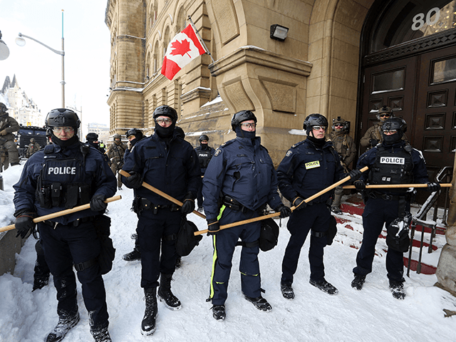 A line of police officers pushes past the offices of the Prime Minister Justin Trudeau as they move to remove protesters on February 19, 2022 in Ottawa, Canada. - Police pushed into downtown Ottawa Saturday in a bid to dislodge several hundred dug-in protesters and big rigs that have choked …