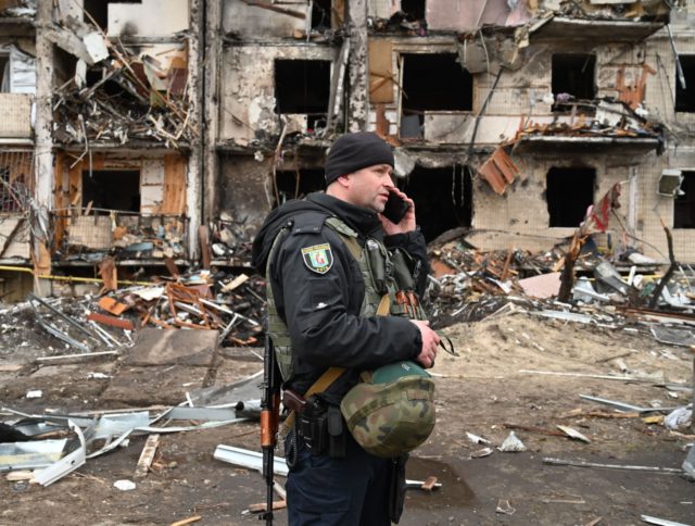 A police officer stands guard at a damaged residential building at Koshytsa Street, a suburb of the Ukrainian capital Kyiv, where a military shell allegedly hit, on February 25, 2022. - Invading Russian forces pressed deep into Ukraine as deadly battles reached the outskirts of Kyiv, with explosions heard in …