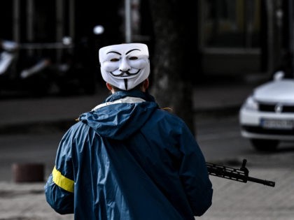 A member of Ukrainian forces, wearing Guy Fawkes mask (Anonymous mask), patrols downtown Kyiv, on February 27, 2022. - Kyiv authorities on February 26, 2022 toughened curfew orders in the city, saying violators would be considered "enemy" saboteurs as Russian forces press to capture Ukraine's capital. (Photo by Aris Messinis …