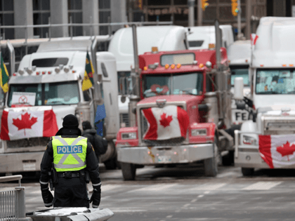 A police officer stands guard near trucks participating in a blockade of downtown streets near the parliament building as a demonstration led by truck drivers protesting vaccine mandates continues on February 16, 2022 in Ottawa, Ontario, Canada Prime Minister Justin Trudeau has invoked the Emergencies Act for the first time …