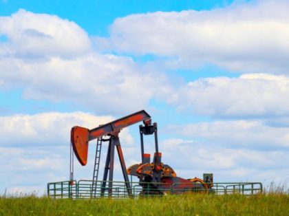 Colorful pump jack on oil well - low horizon on prairie with green grass and wild flowers - big blue cloudy sky - room for text
