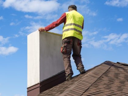 Professional workman standing roof top and measuring chimney of new house under constructi