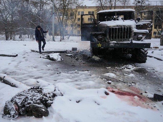 The body of a serviceman is coated in snow as a man takes photos of a destroyed Russian military multiple rocket launcher vehicle on the outskirts of Kharkiv, Ukraine, Friday, Feb. 25, 2022. Russian troops bore down on Ukraine's capital Friday, with gunfire and explosions resonating ever closer to the …