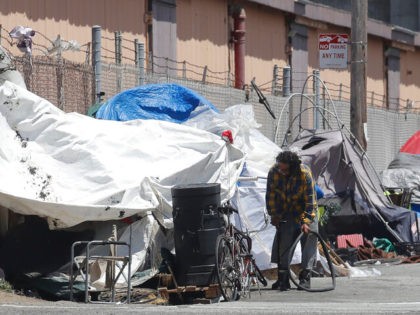 This Thursday, June 27, 2019, photo shows a man holding a bicycle tire outside of a tent along a street in San Francisco. (AP Photo/Jeff Chiu)
