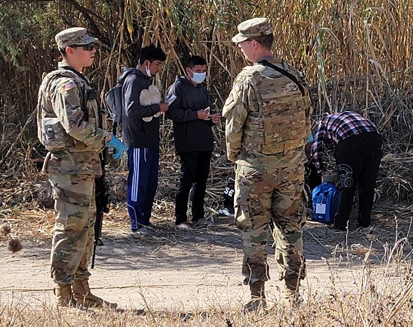 Texas National Guardsmen stand watch over a group of migrants in Eagle Pass while waiting for Border Patrol agents. (Bob Price/Breitbart Texas)