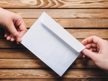 White envelope in the hands of two people on a wooden background.