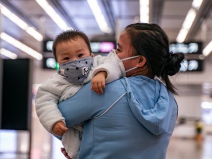 HONG KONG, CHINA - JANUARY 29: A woman carries a baby wearing a protective mask as they exit the arrival hall at Hong Kong High Speed Rail Station on January 29, 2020 in Hong Kong, China. Hong Kong government will deny entry for travellers who has been to Hubei province …