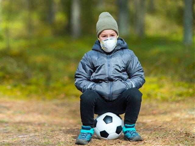Little boy with a mask and soccer ball in the park. Corona virus quarantine
