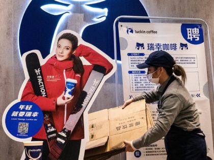 WUHAN, CHINA - FEBRUARY 8: (CHINA OUT) People sit drinking coffee near a model of freestyle skiing gold medalist Eileen Gu who competes for China, at Luckin Coffee on February 8, 2022 in Wuhan, Hubei, China. Eileen Gu, who was born in the United States in 2003, began to represent …