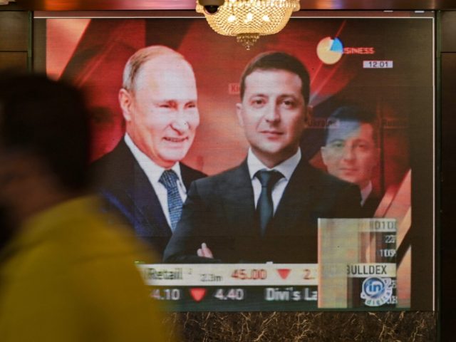 A man walks past a digital broadcast screen airing news of the conflict between Russia and