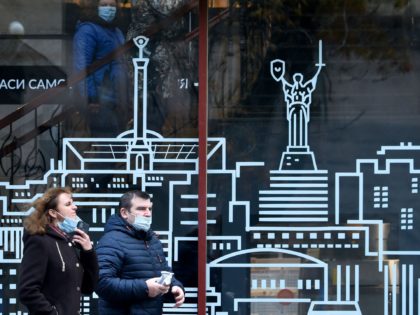 A couple, wearing a protective face mask, walk past shop window decorated with stylized vi